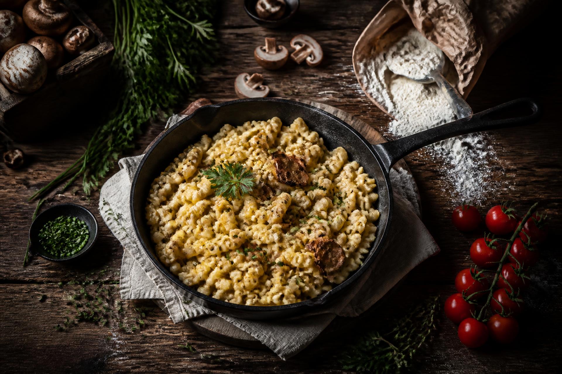 Pfanne mit Kräuterspätzle, frischen Champignons und Cocktailtomaten auf Holztisch